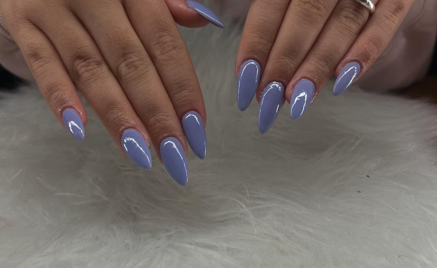 Long almond nails in one glossy periwinkle blue on every nail, hands held over white fur.